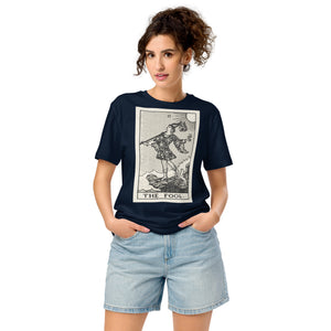 Mid-light organic cotton t-shirt featuring The Fool tarot card with cliff, dog, and sun in high-contrast woodcut rendering.