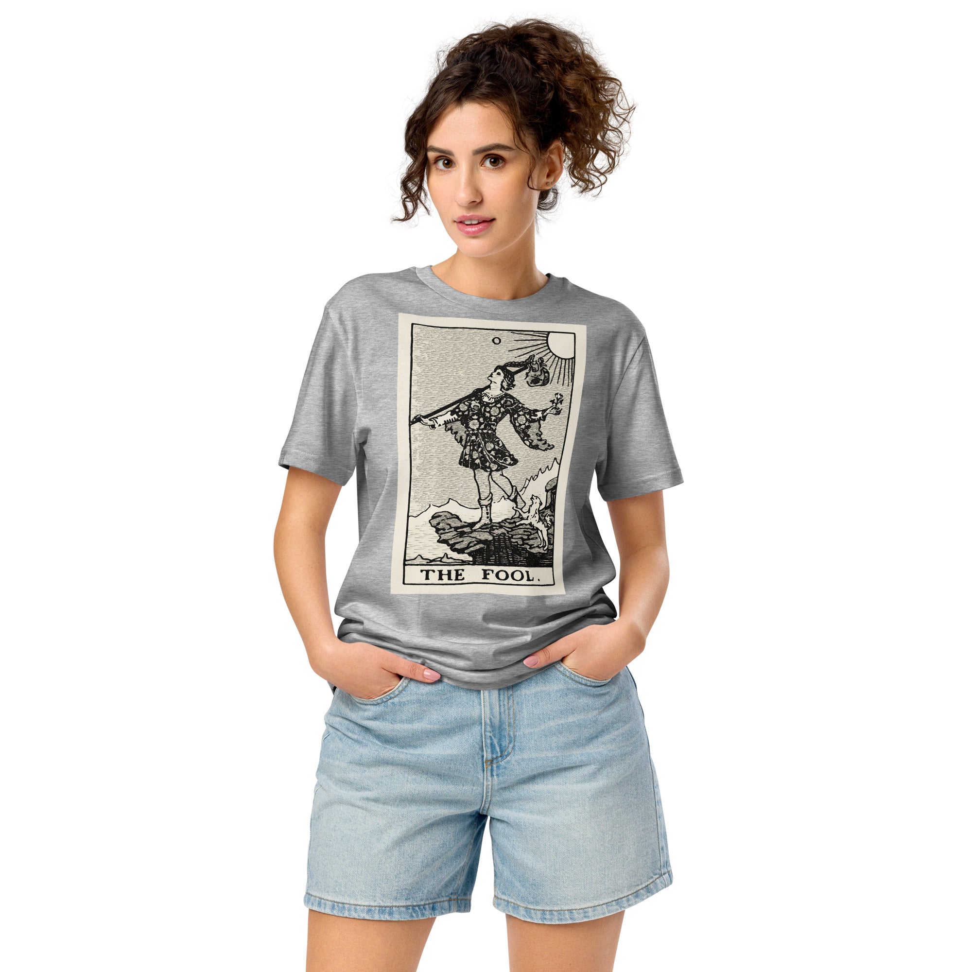 Mid-light organic cotton t-shirt featuring The Fool tarot card with cliff, dog, and sun in high-contrast woodcut rendering.