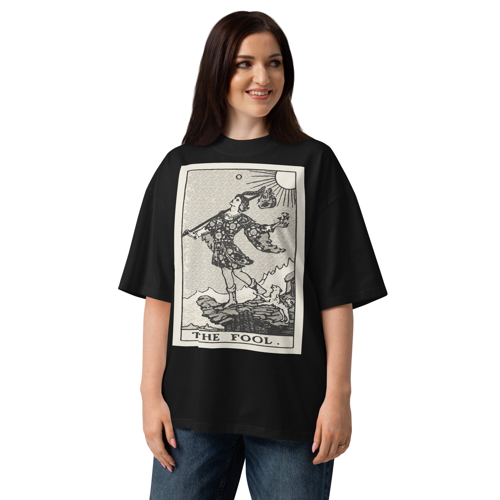 Oversized organic cotton t-shirt displaying The Fool tarot card with cliff, dog, and rising sun in modern woodcut style.